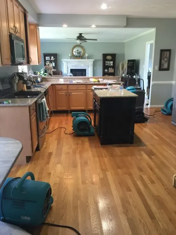 Air movers drying a kitchen floor and hardwood boards after a leak
