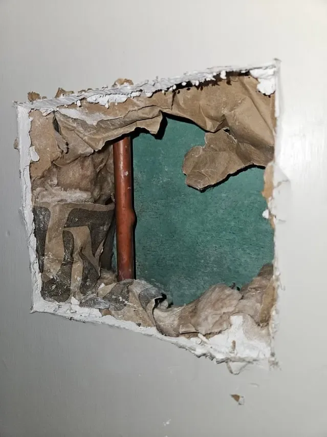 Drywall opened to reach a leaking copper pipe inside the wall