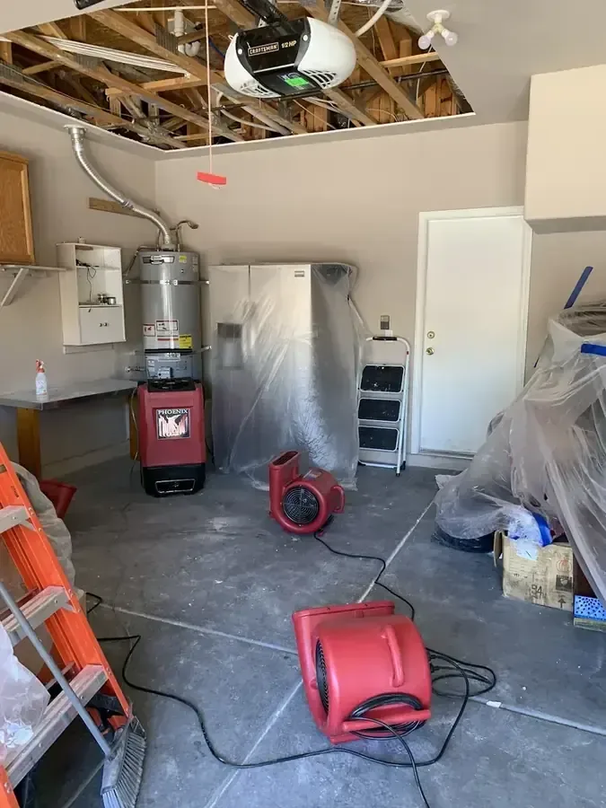 Drying equipment set up in a garage with the ceiling opened after a water heater leak