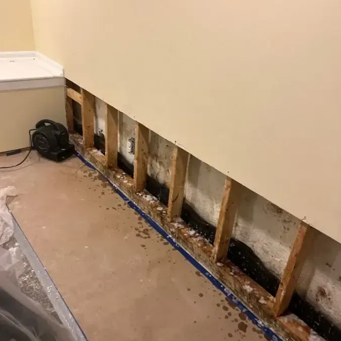 A strip of drywall removed along the bottom of a wall, with plastic sheeting laid across the floor