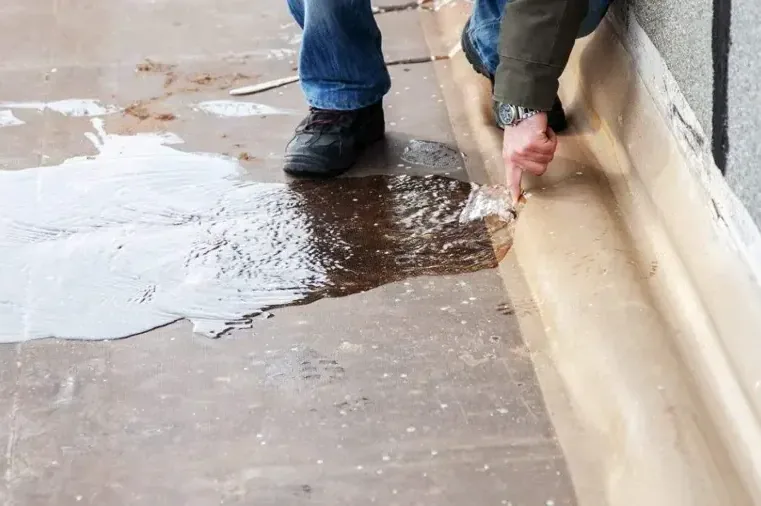 Water pooled on a concrete floor as wet baseboard trim is pulled away from the wall